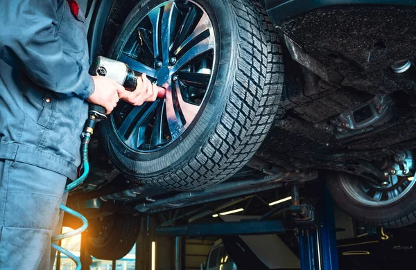 Mécanicien utilisant une clé pneumatique pour retirer un pneu d'une voiture élevée sur un ascenseur dans un garage équipé de moteurs. allo gom auto Lille