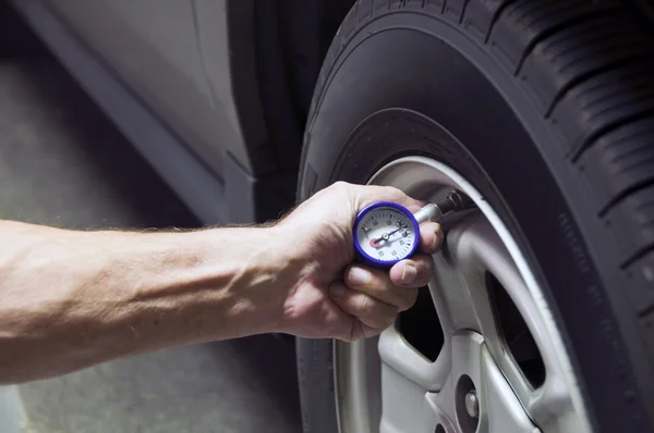 Une personne vérifie la pression des pneus à l'aide d'une jauge située sur la roue d'un véhicule, près du moteur.