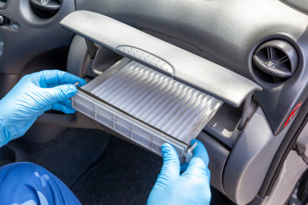 Des mains en gants bleus effectuent méticuleusement des réparations automobiles en installant un filtre d'habitacle dans la boîte à gants d'une voiture.