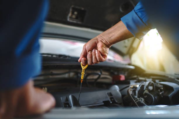 Personne vérifiant le niveau d'huile moteur avec une jauge dans le capot ouvert d'une voiture, se préparant à une révision de vidange moteur.